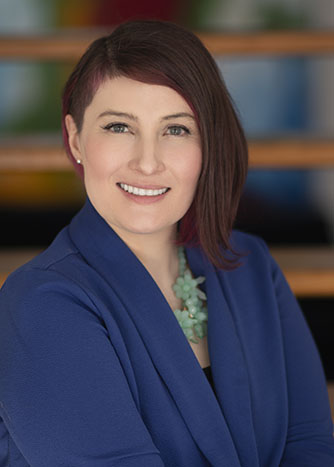 Photo of Tomiyo Stoner smiling in front of a wooden staircase